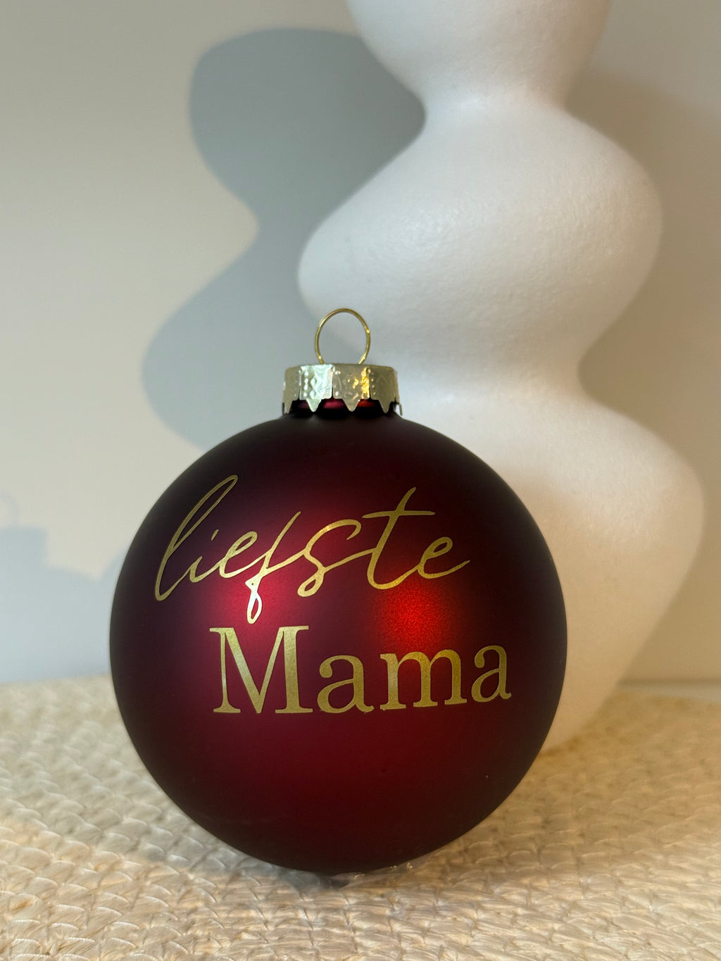 Detail van een matte bordeauxrode kerstbal met sierlijke goudkleurige tekst Liefste mama.