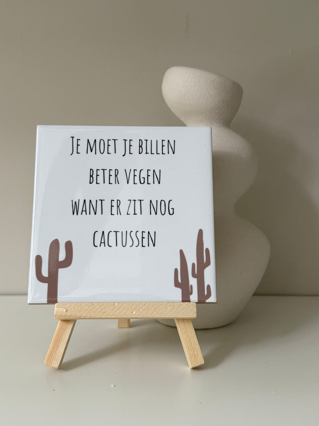 Grappig cactus tegeltje van keramiek met tekst en bruine cactussen, op houten standaard voor een witte vaas.