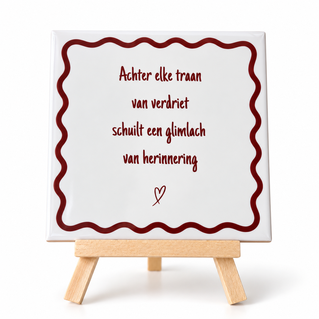 Beige keramieken herinneringstegeltje met bordeauxrode tekst en sierlijke rand op houten houdertje tegen witte achtergrond.