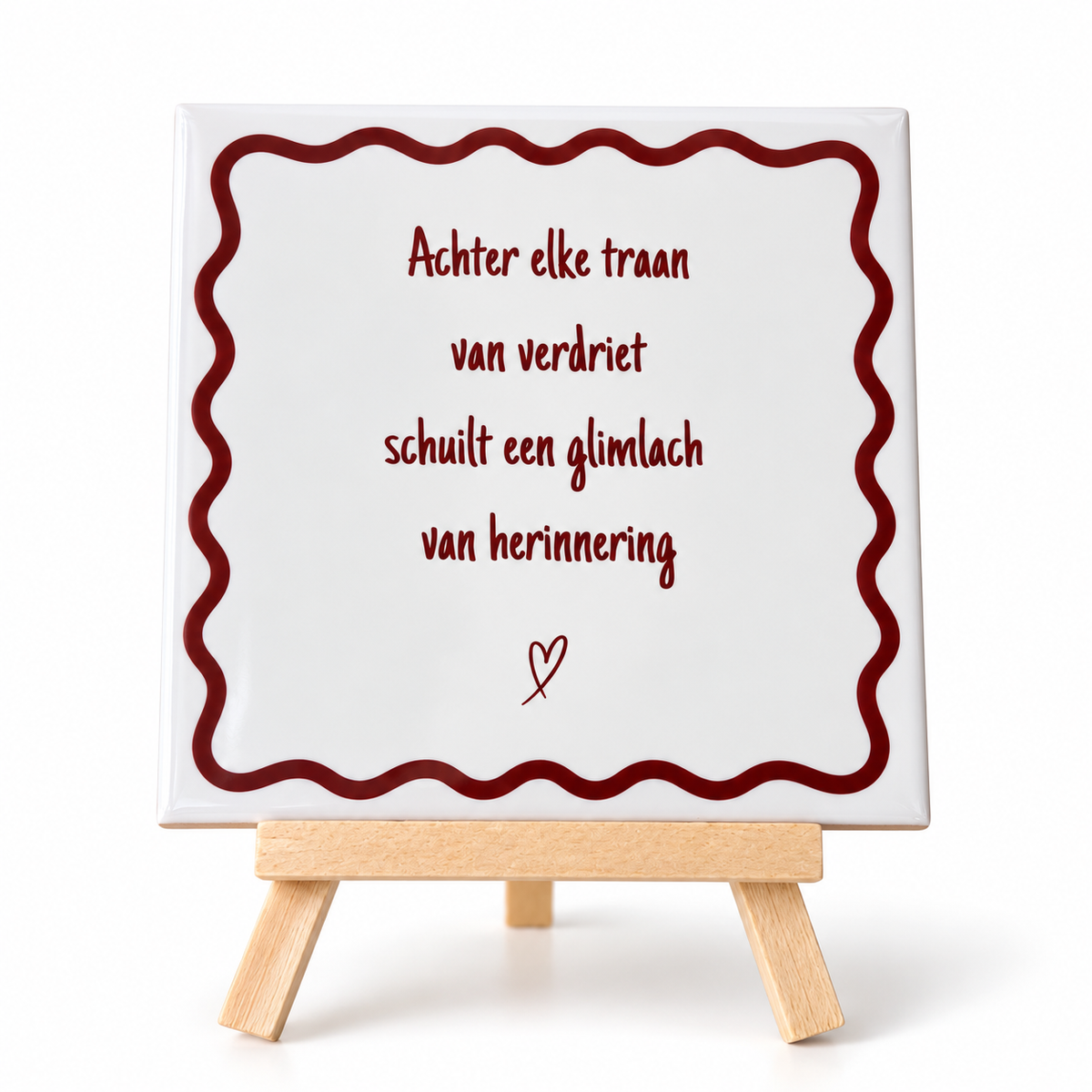 Beige keramieken herinneringstegeltje met bordeauxrode tekst en sierlijke rand op houten houdertje tegen witte achtergrond.