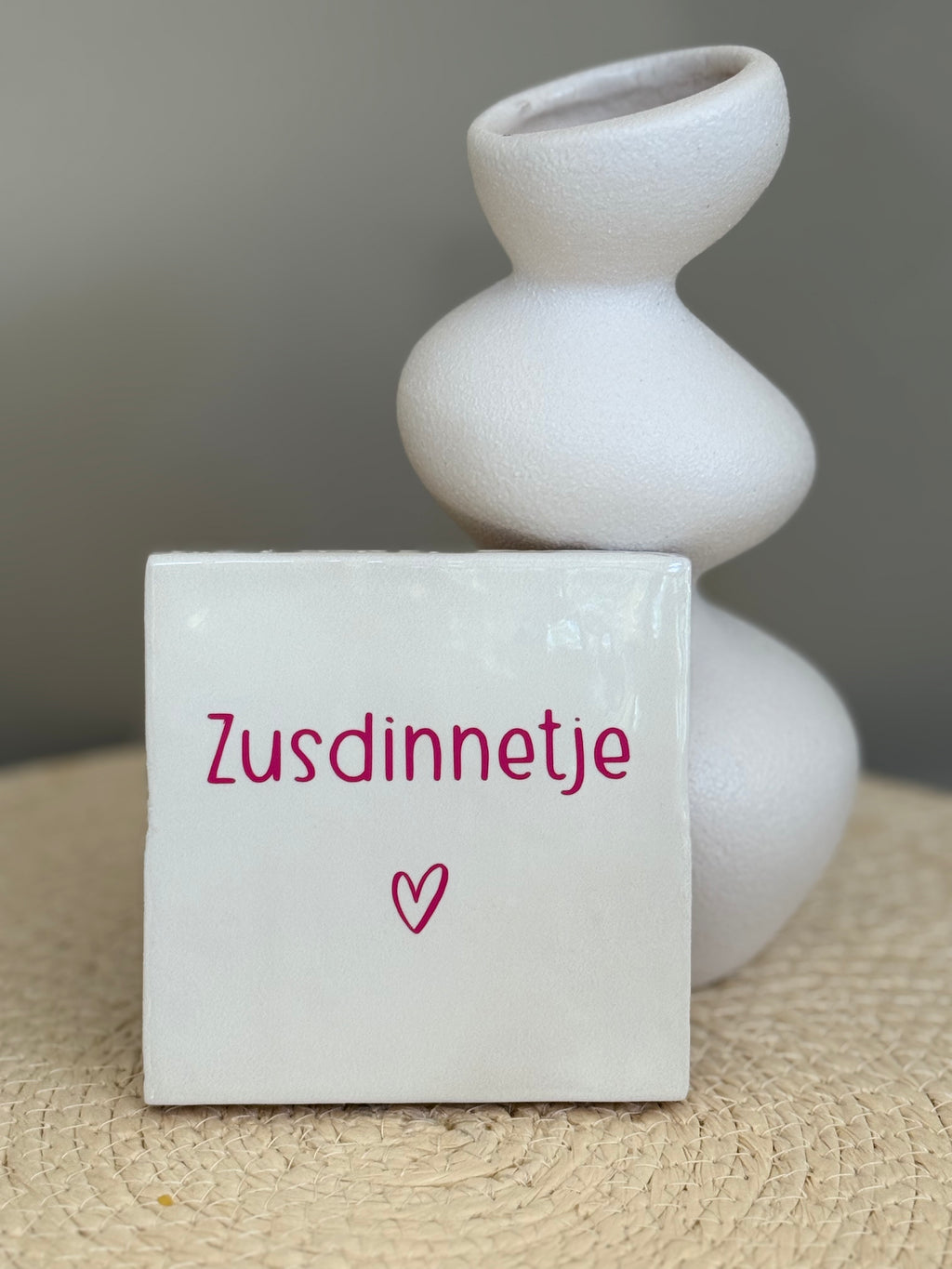 Wit Zusdinnetje tegeltje met roze tekst en hartje, staand naast een witte decoratieve vaas.